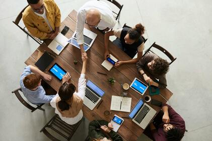 Aerial view of collaborators around a table. Several laptopls opened. Shaking hands. 